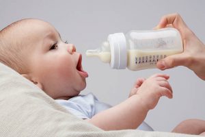 Bébé la bouche grande ouverte en train d'être nourri au biberon