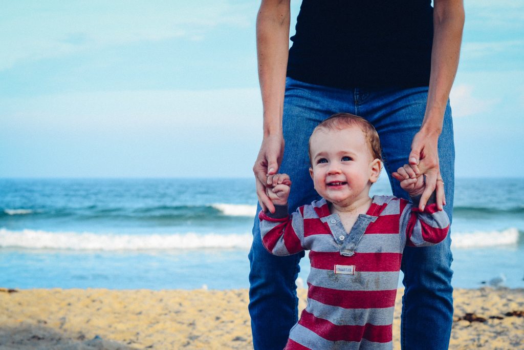 Un bébé sur la plage en train de marcher avec son père